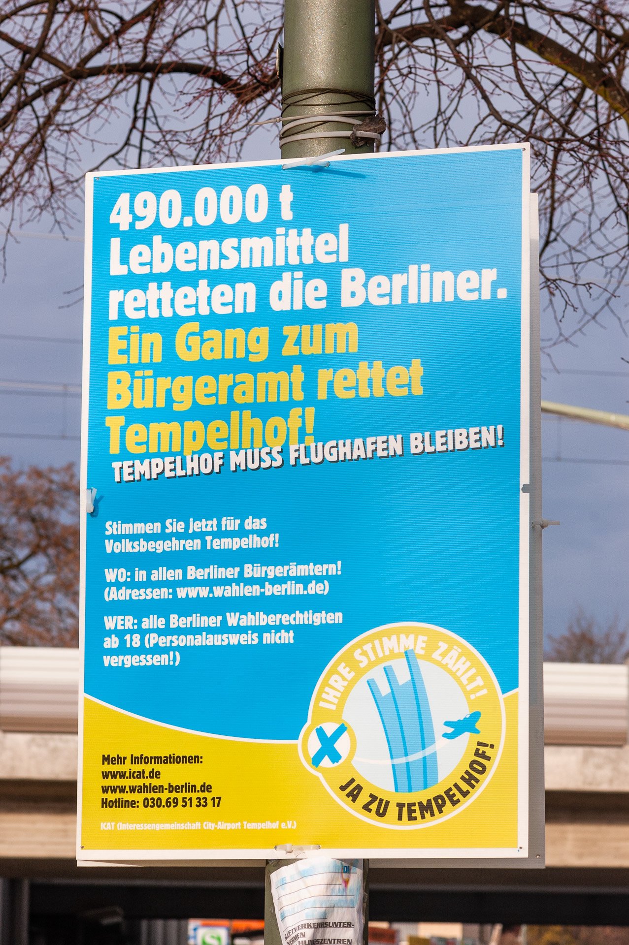 Farbbild: Plakat zum Volksbegehren an einem Pfahl in Berlin-Lankwitz, Leonorenstraße: ›Tempelhof muss Flughafen bleiben!‹ Im Hintergrund eine Eisenbahnbrücke. (Foto: Martin Frech, 1/2008)